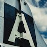 The vertical stabilizer of an aircraft displaying a large letter A against a partly cloudy sky.