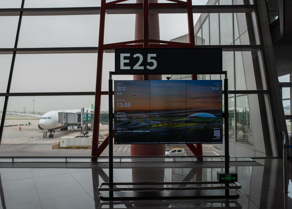 A jet bridge connected to an airplane at an airport gate, with a digital sign displaying flight information.