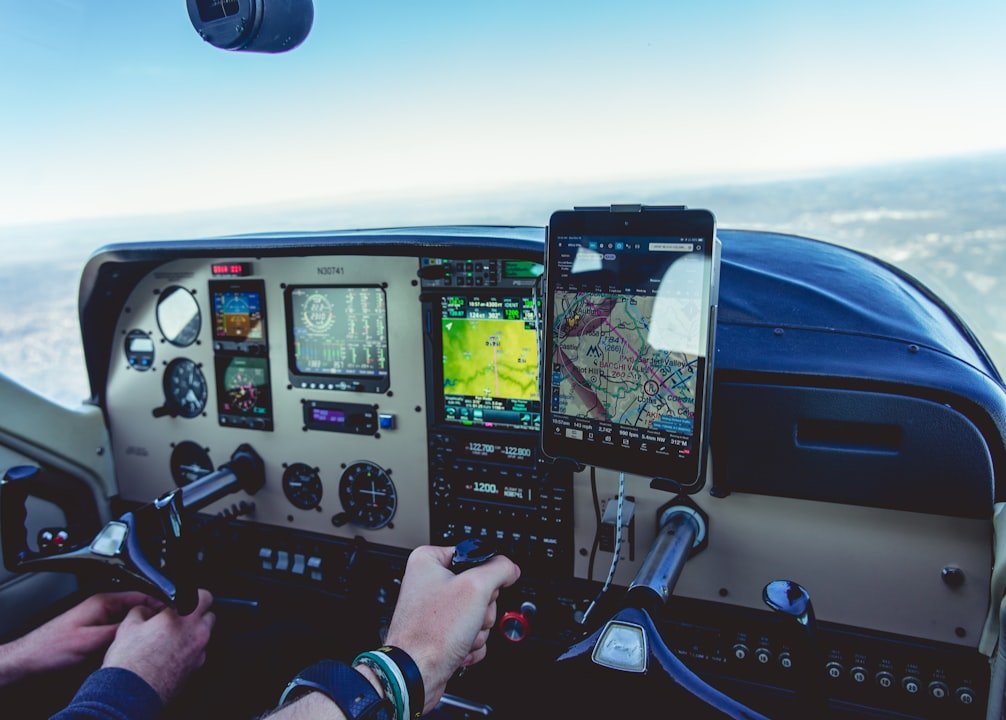 An airplane cockpit with controls and gauges, a hand on the control yoke and a tablet showing a digital map.
