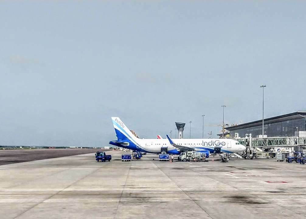 A busy airport apron with a passenger aircraft parked near the terminal, boarding bridges and ground service equipment.