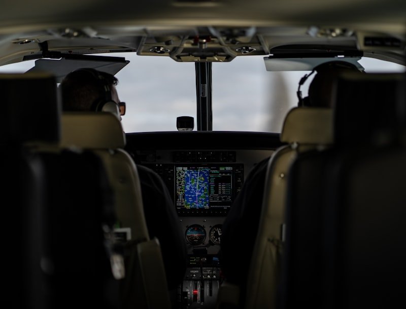 Two pilots seated in an aircraft cockpit wearing headsets, with controls, screens and instruments in front of them.